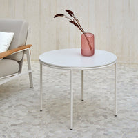 Round white coffee table with sleek metal legs, paired with a textured beige floor and soft pastel decor.