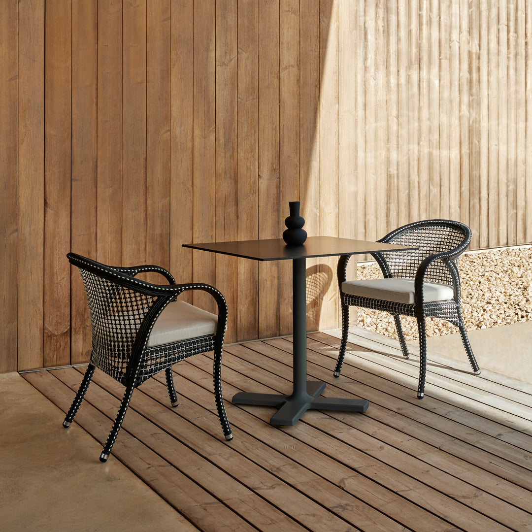 Black wicker chairs with cream cushions beside a sleek black table on a wooden deck. Warm, natural tones throughout.