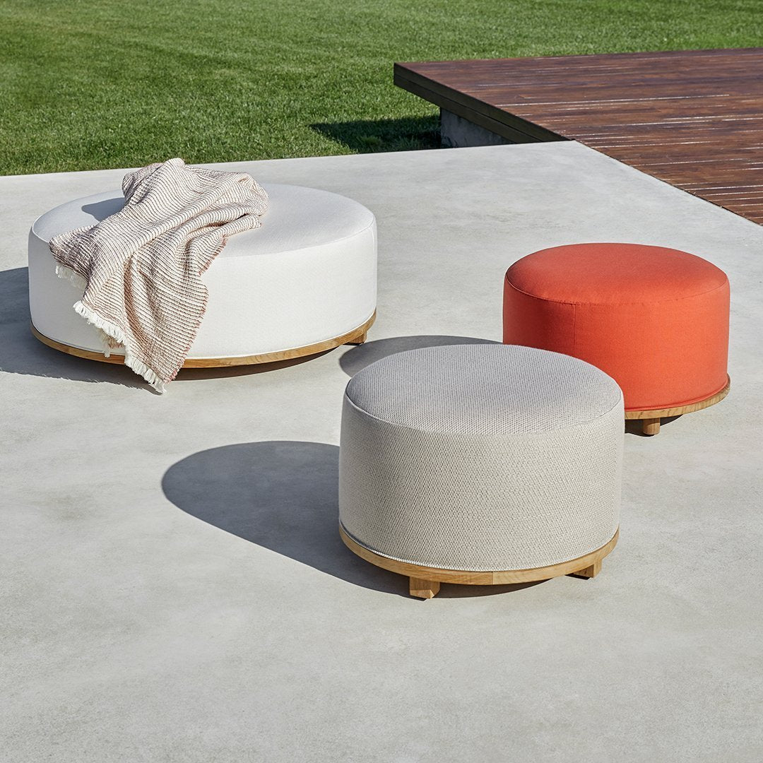 Round ottomans in white, light gray, and vibrant orange, featuring a smooth fabric finish and a subtle wooden base.