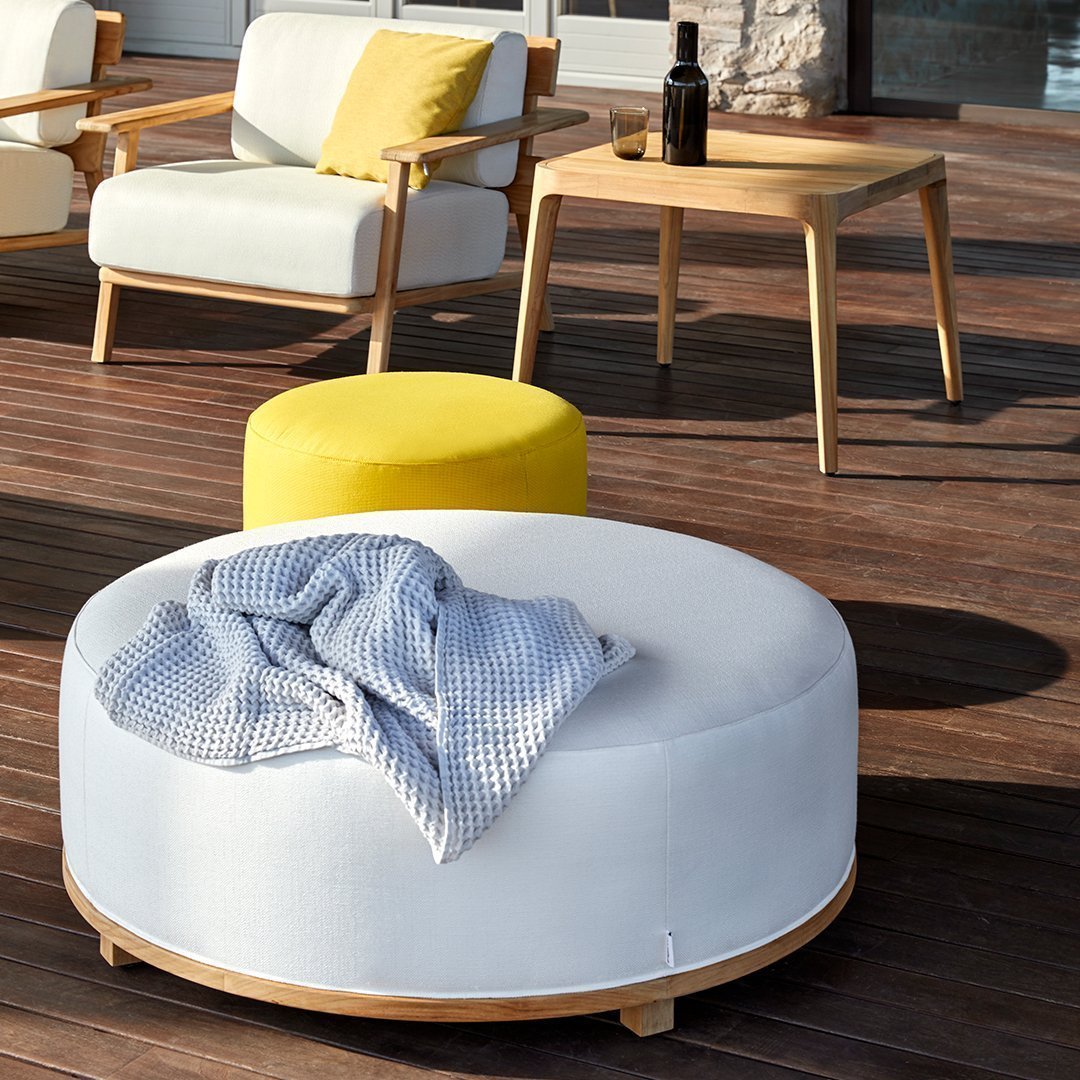 Round white ottoman with a blue blanket, paired with a bright yellow pouf on a wooden patio. Modern and vibrant colors.