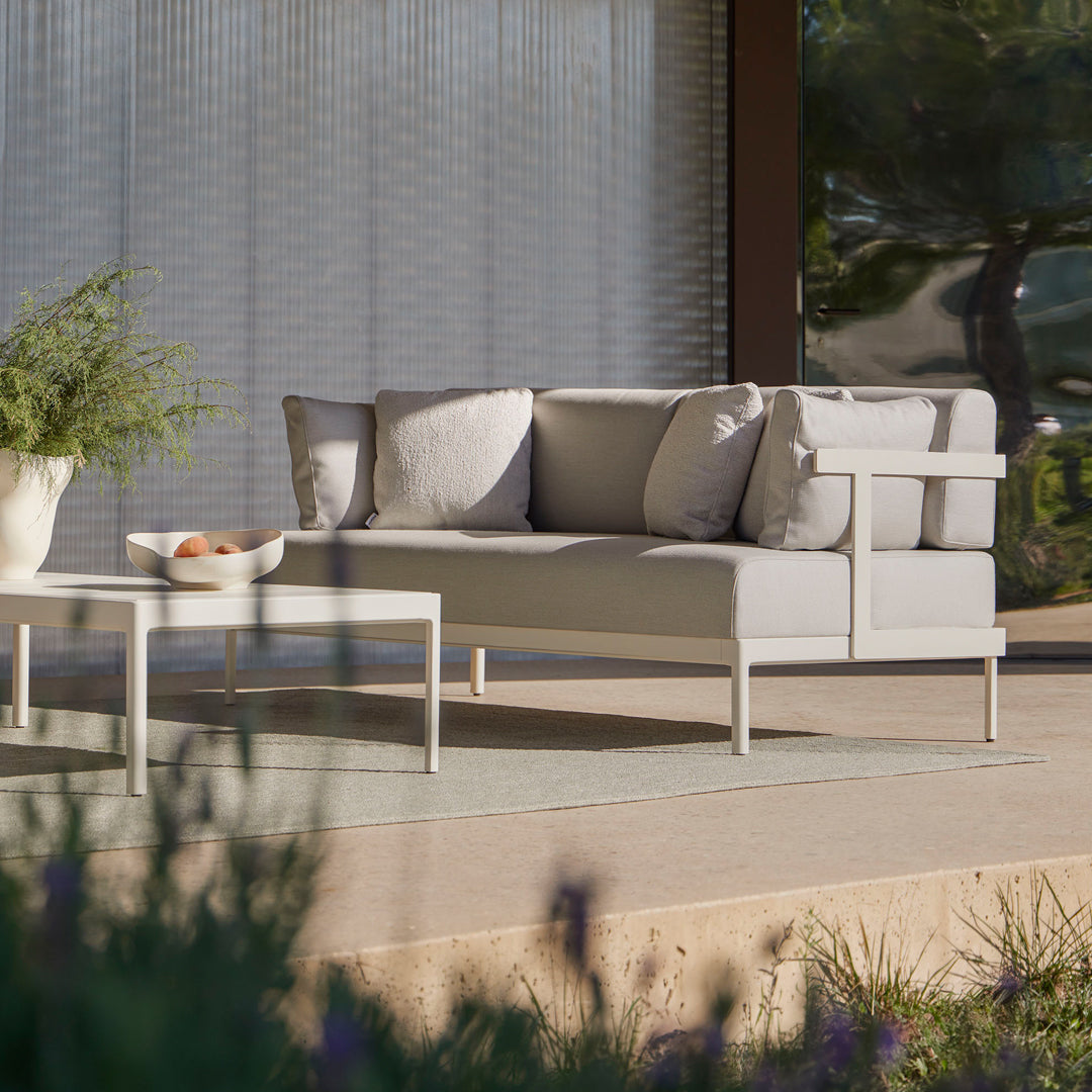 Contemporary gray outdoor sofa with soft cushions, complemented by a minimalist white coffee table on a textured patio.