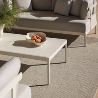 Light grey sofa and white table on a textured beige rug, featuring natural tones and minimalist design elements.