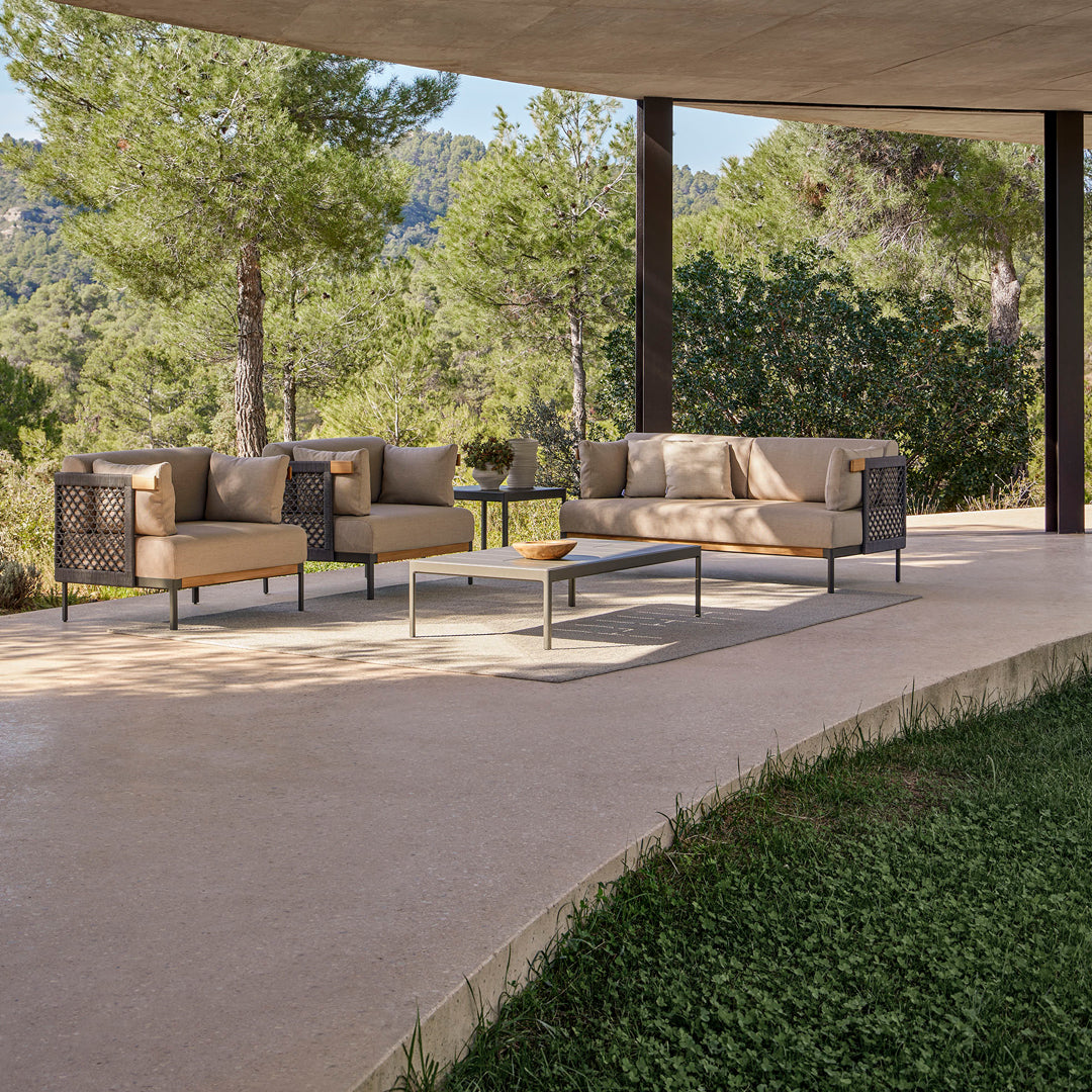 Beige outdoor sofa set with dark woven accents, featuring neutral cushions and a minimalist table against a green backdrop.