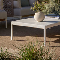 "Modern white coffee table on a natural textured surface with greenery, perfect for outdoor settings."