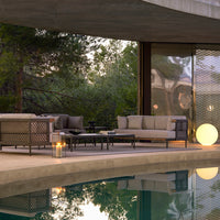 Modern outdoor seating set with neutral beige cushions and black frame, surrounded by greenery and reflecting pool.