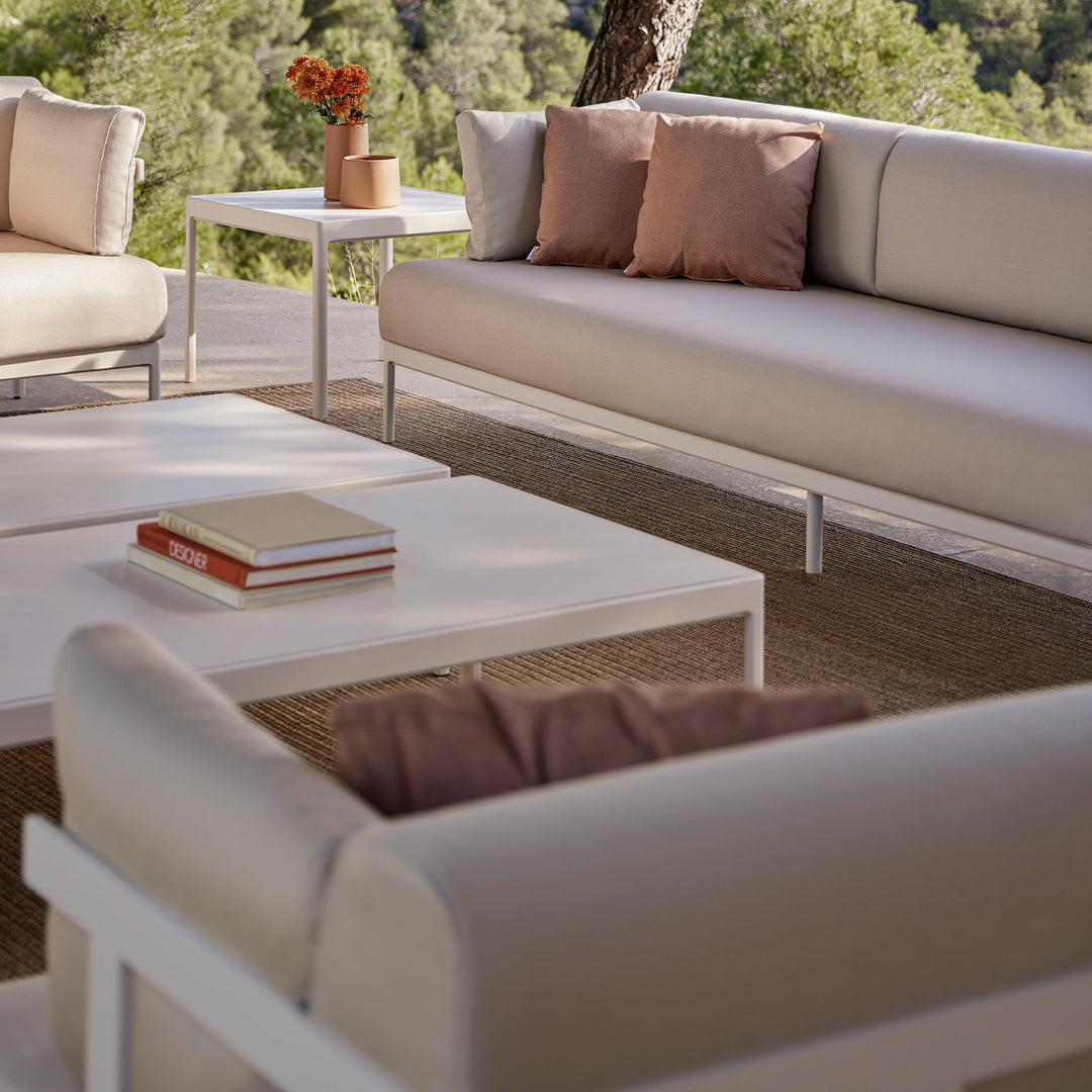 Neutral-toned outdoor sofa set with soft beige cushions and blush pink accent pillows on a light wooden deck.
