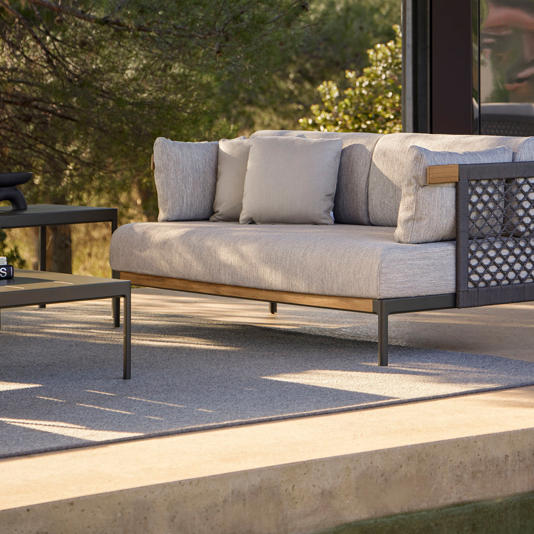 Light gray sofa with textured cushions and a dark metal frame, complemented by a matching gray table on a neutral patio surface.