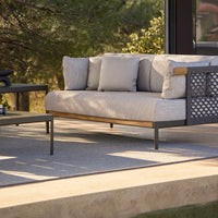 Light gray sofa with textured cushions and a dark metal frame, complemented by a matching gray table on a neutral patio surface.