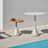 Modern white and natural wood tables with sleek cone bases, set against a minimalist backdrop and vibrant blue pool.