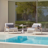 Modern outdoor seating set featuring gray cushions, wooden accents, and a minimalist white table by a sparkling blue pool.