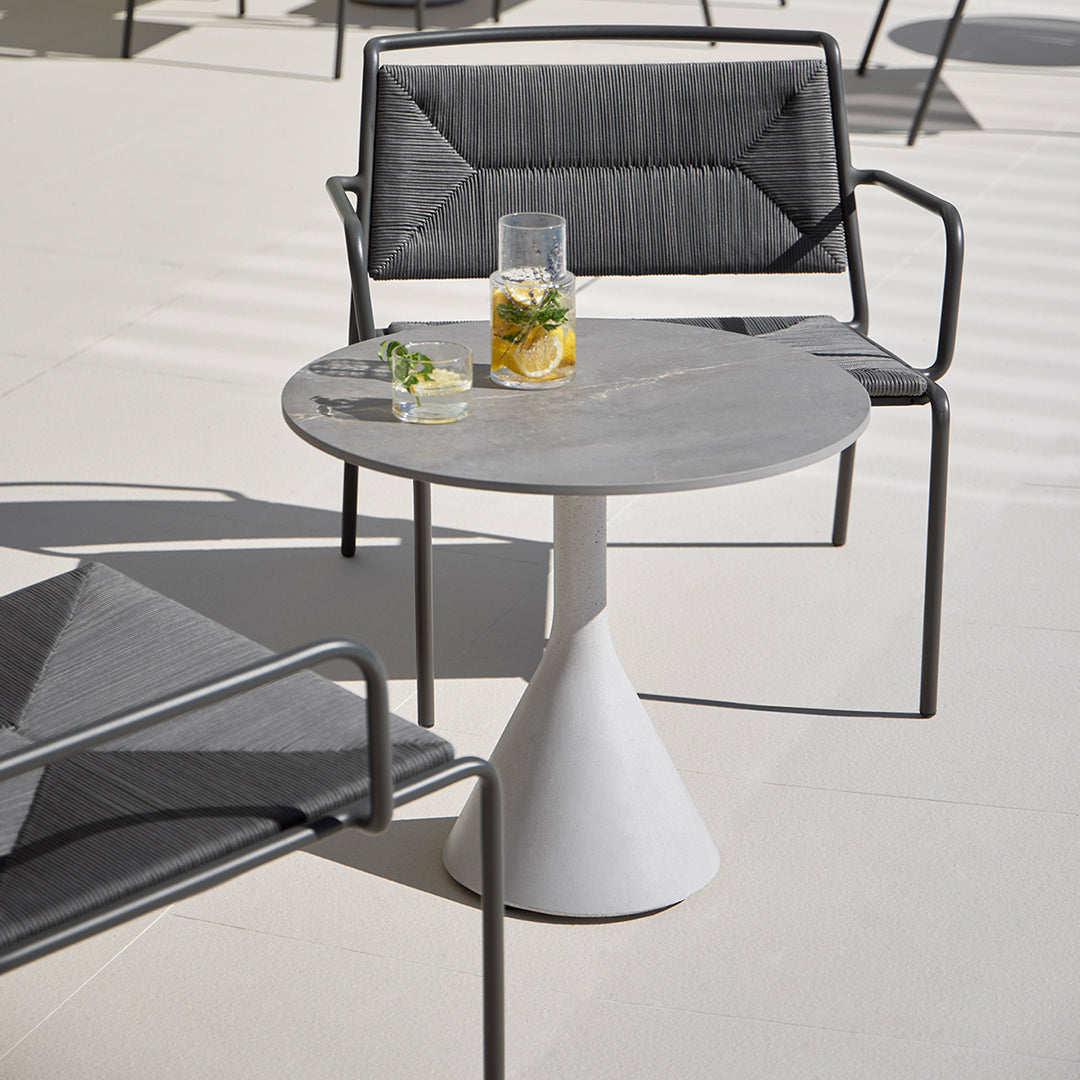 Gray round table with a white pedestal, complemented by black textured chairs. Modern outdoor color palette.