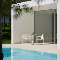 Minimalist white outdoor furniture against a backdrop of green landscape and blue pool water, creating a serene atmosphere.