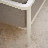 Light gray fabric sofa with a sleek white frame, set against a textured stone floor.