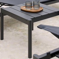 Black outdoor side table with slatted top, featuring a wooden tray and transparent glassware on a light stone surface.