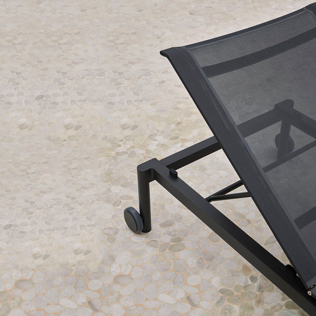 Black mesh lounge chair with a sleek frame, set against a textured light-colored floor.