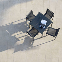 Black mesh chairs and slatted table set against a light beige tiled surface, casting soft shadows.