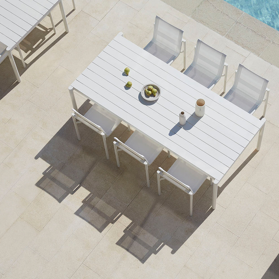 White outdoor table with sleek modern design, complemented by light gray chairs on a sunlit patio.