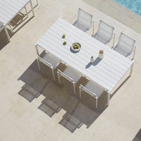 White outdoor table with sleek modern design, complemented by light gray chairs on a sunlit patio.