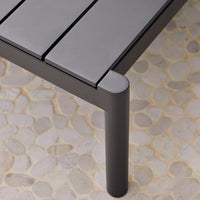 Black slatted tabletop with smooth edges, set against a light, textured stone background.