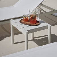 White outdoor side table with minimalist slatted design, paired with refreshing drinks on a wooden tray.