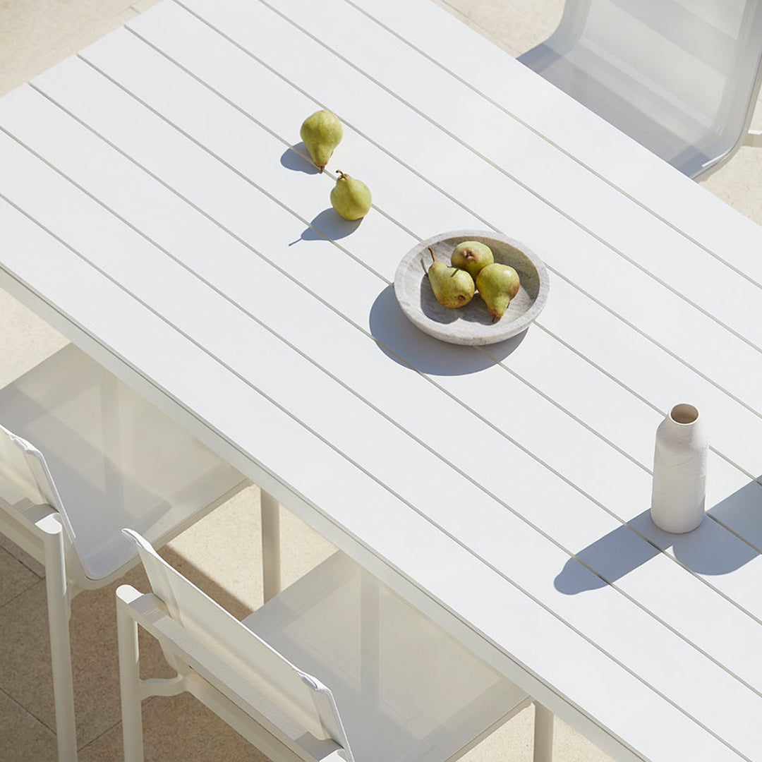 Modern white rectangular table with a slatted design, featuring green pears and a neutral bowl. Minimalist aesthetic.