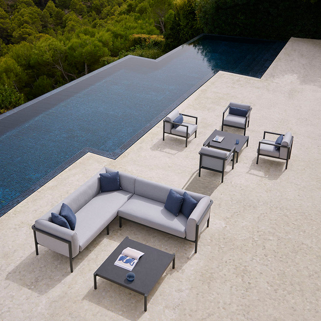 Gray outdoor sectional sofa with blue cushions, alongside matching chairs and tables, set by a sleek poolside.