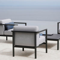Modern outdoor furniture featuring gray cushions and black frames, set against a serene waterfront backdrop.