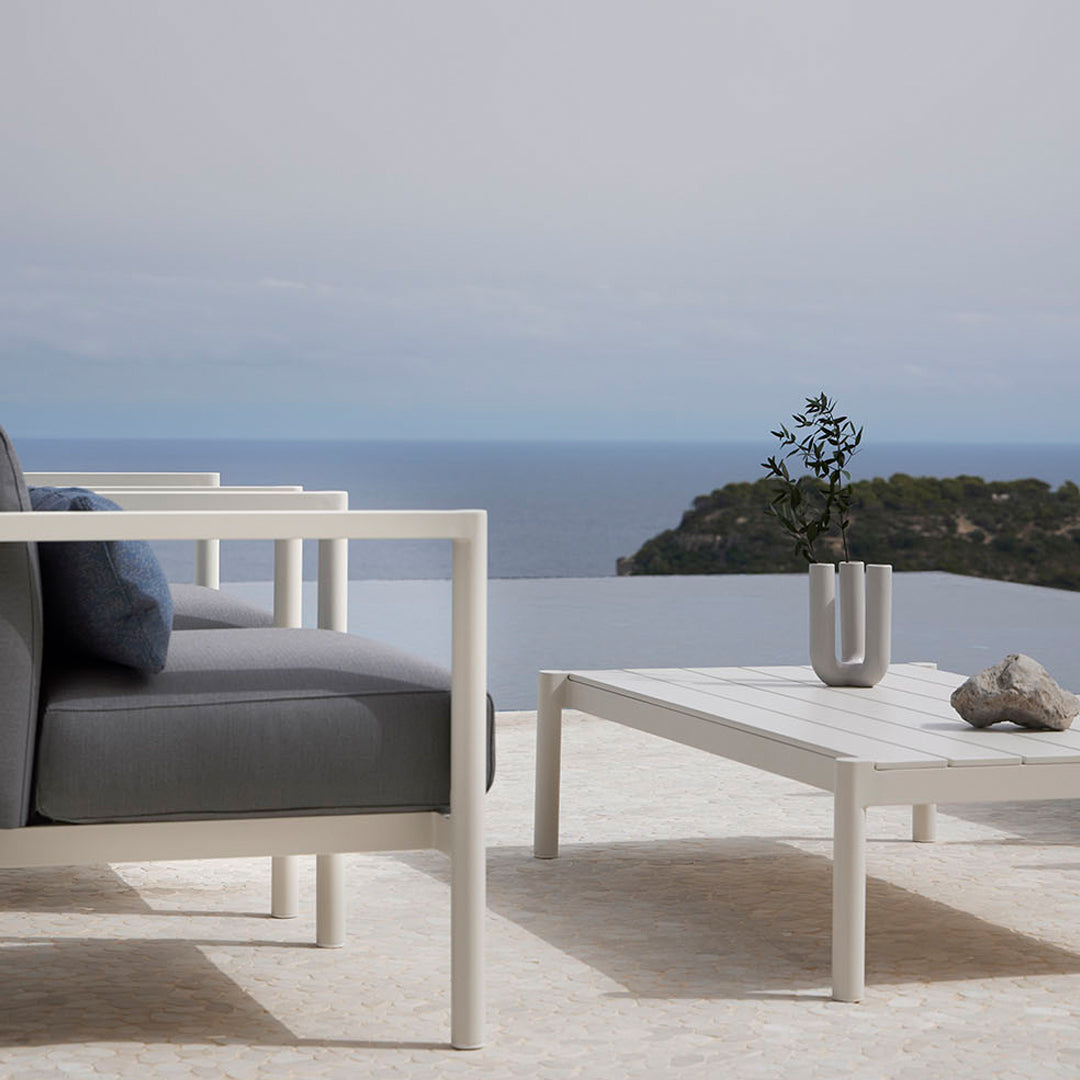 Modern white outdoor furniture with gray cushions, set against a serene ocean backdrop. Elegant, minimalist design.