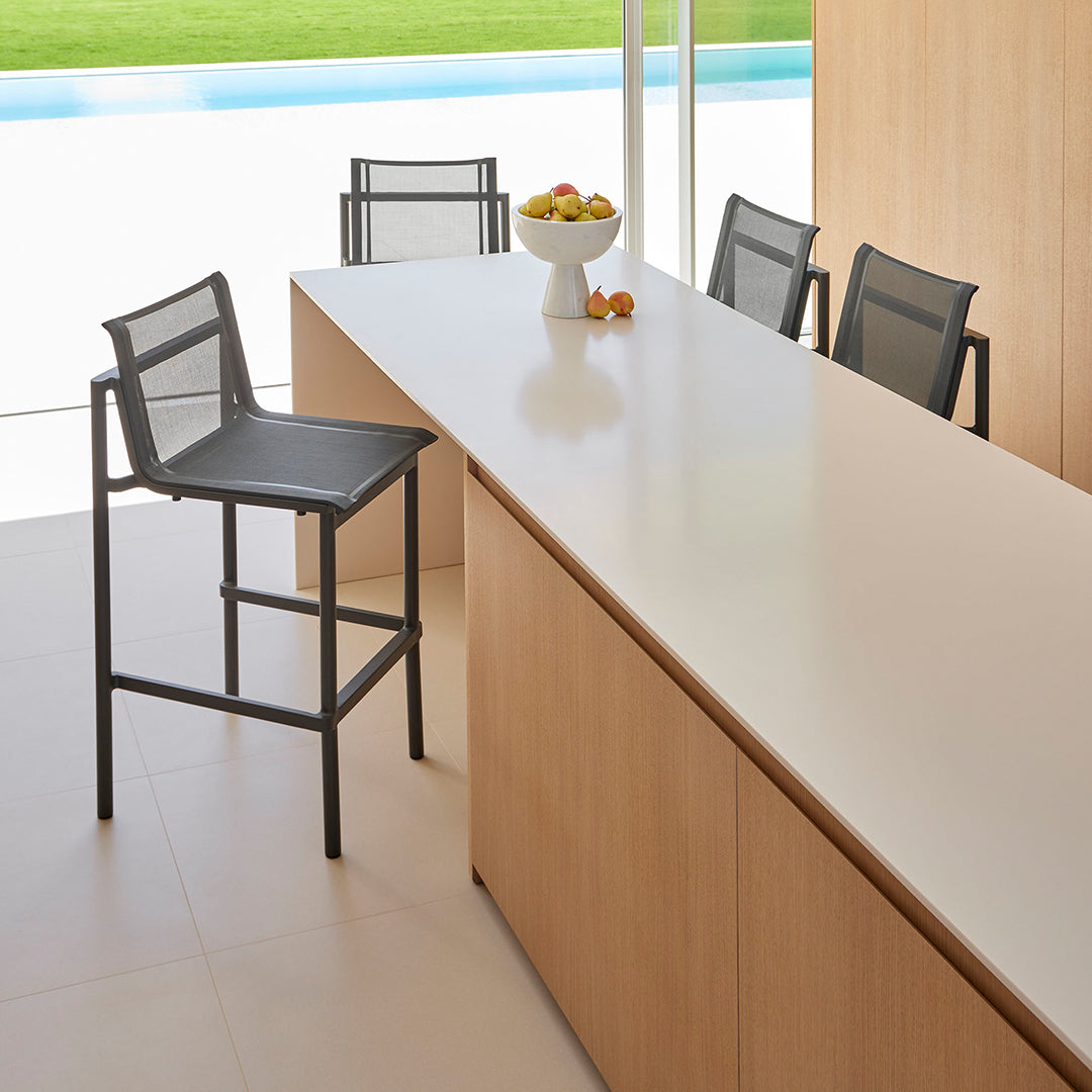 Modern black metal bar stool beside a sleek white countertop, accented by wood cabinetry and green outdoor views.
