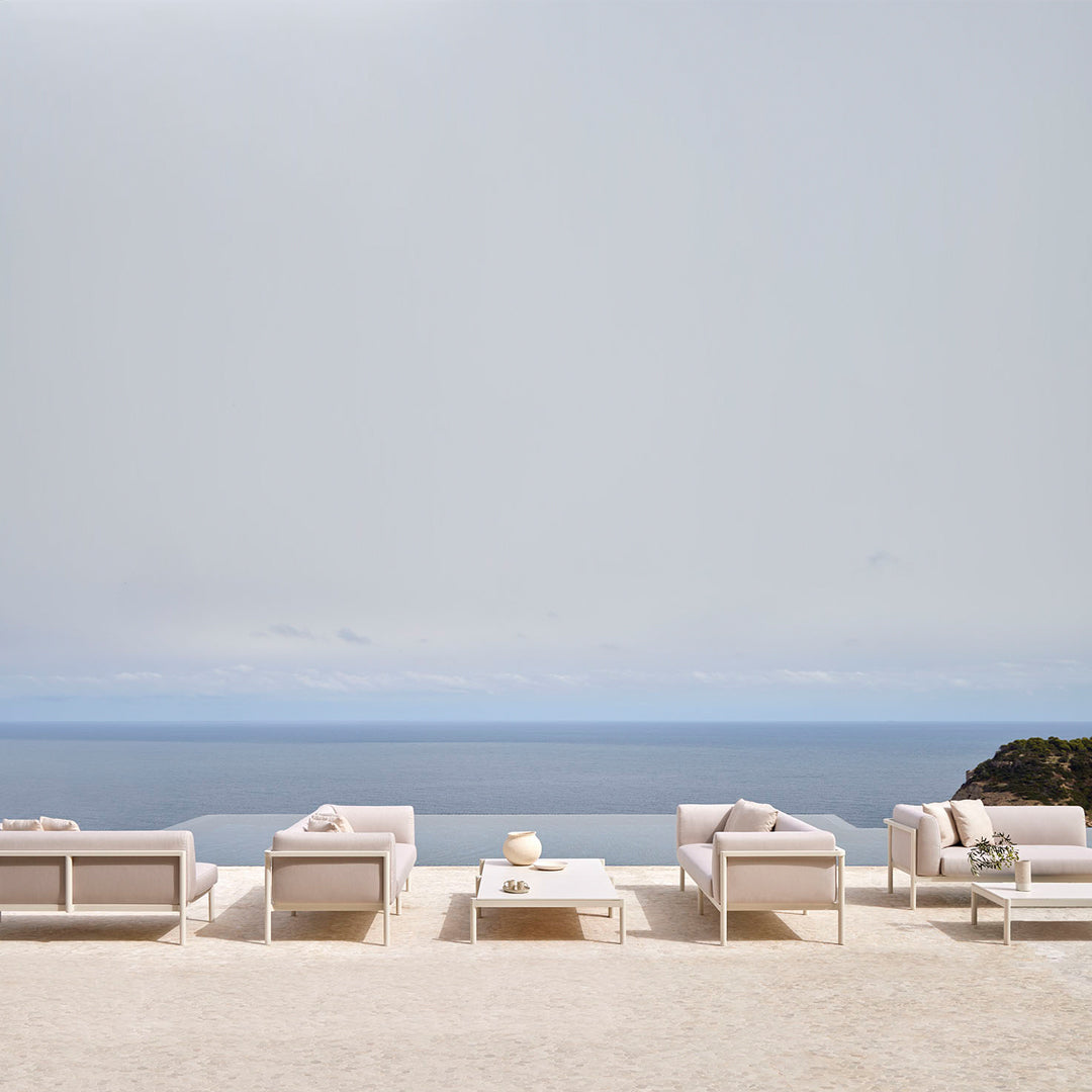 "Minimalist outdoor lounge set in soft beige tones against a serene blue ocean backdrop."