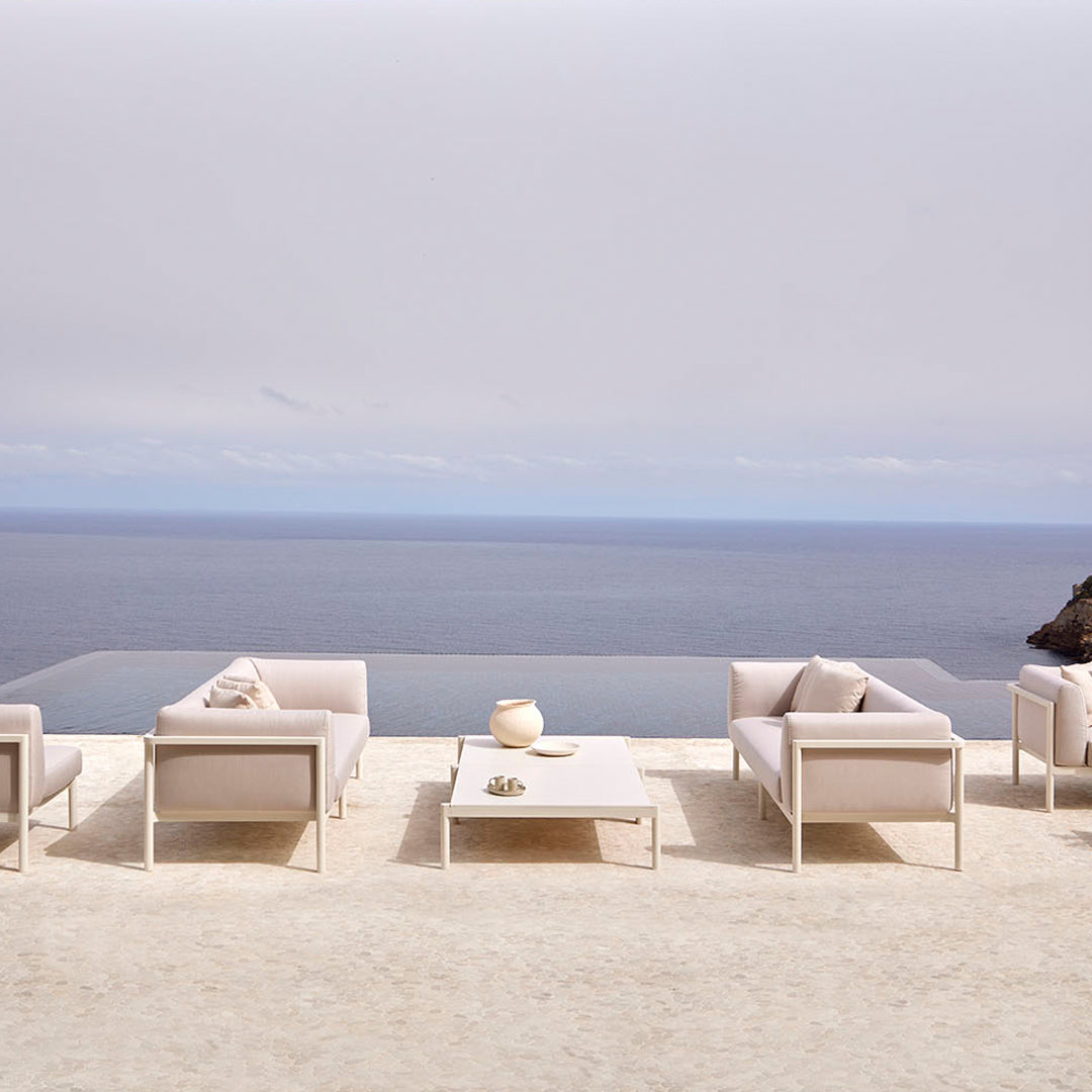 "Light beige outdoor furniture set with a minimalist design against a serene ocean backdrop."