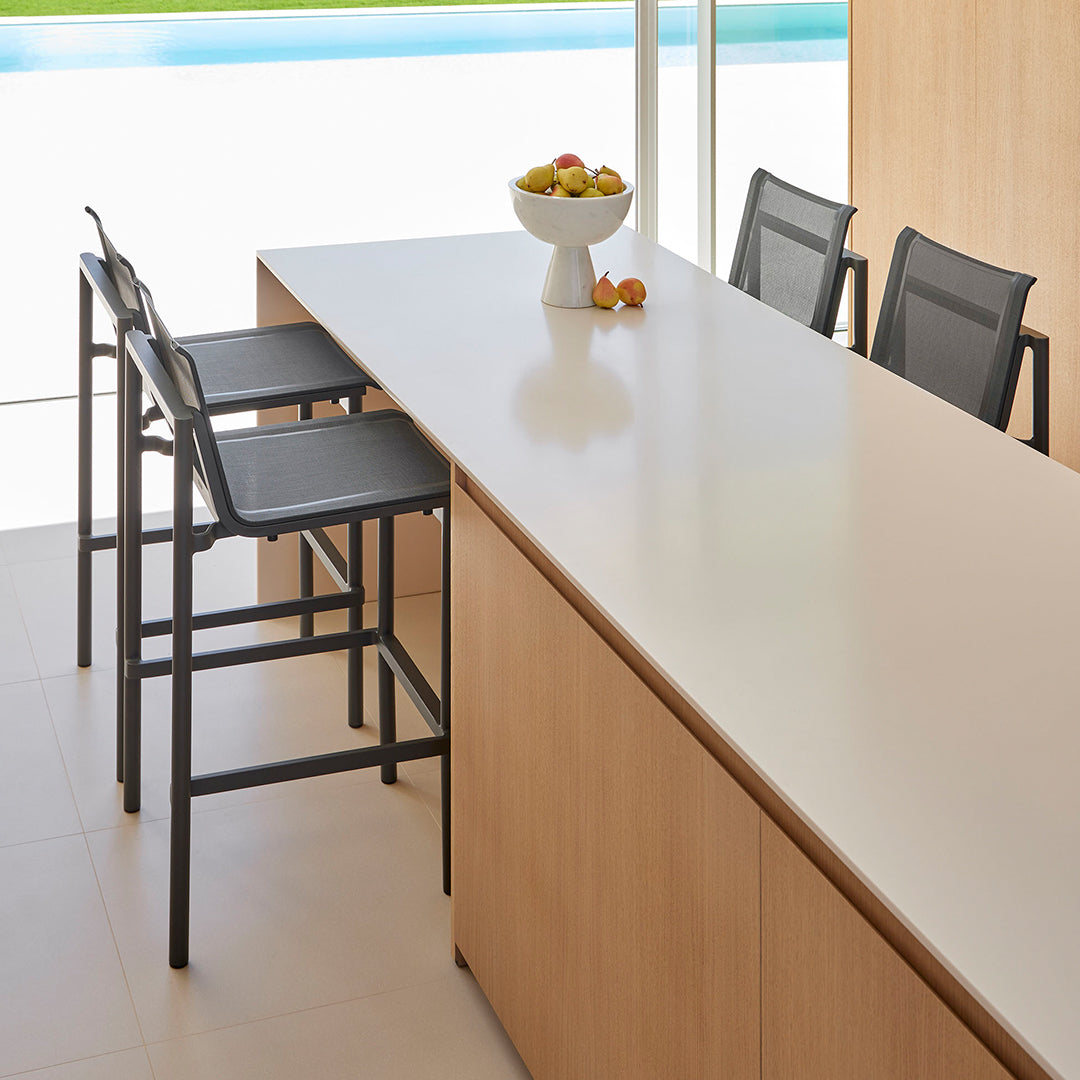"Modern kitchen with light wooden cabinetry, sleek white countertop, and black bar stools."