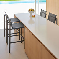 "Modern kitchen with light wooden cabinetry, sleek white countertop, and black bar stools."