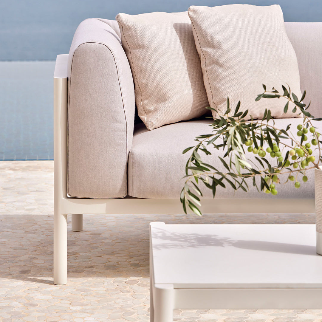 Light beige sofa with cream cushions, paired with a minimalist white table and a touch of greenery.