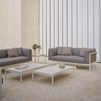 Gray and taupe sofa set with sleek white tables, complemented by neutral-toned decor against a minimalist backdrop.