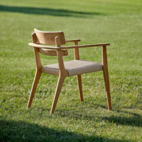 Light wood chair with woven beige seat, featuring a minimalist design and natural finish, set against a green grass backdrop.