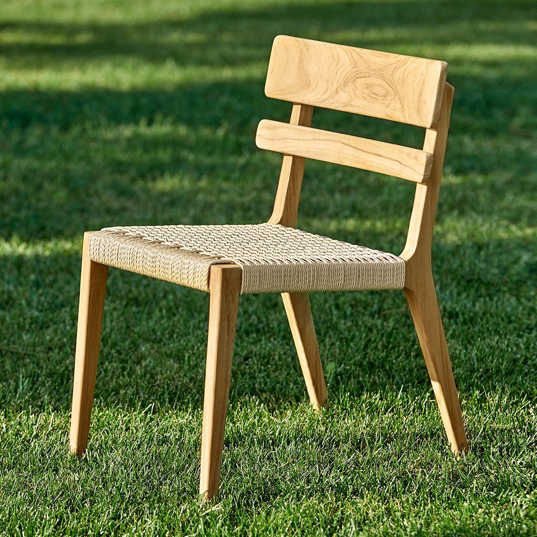 Natural wood chair with a light beige woven seat, showcasing a minimalist design against a green grass backdrop.