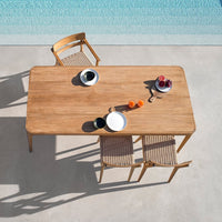 Light wood dining table with natural finish, featuring woven beige chairs and minimalist black and white tableware.