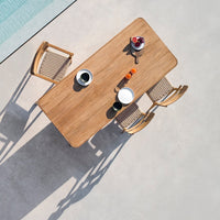 Natural wood dining table with a smooth finish, surrounded by light-colored woven chairs, set against a neutral background.