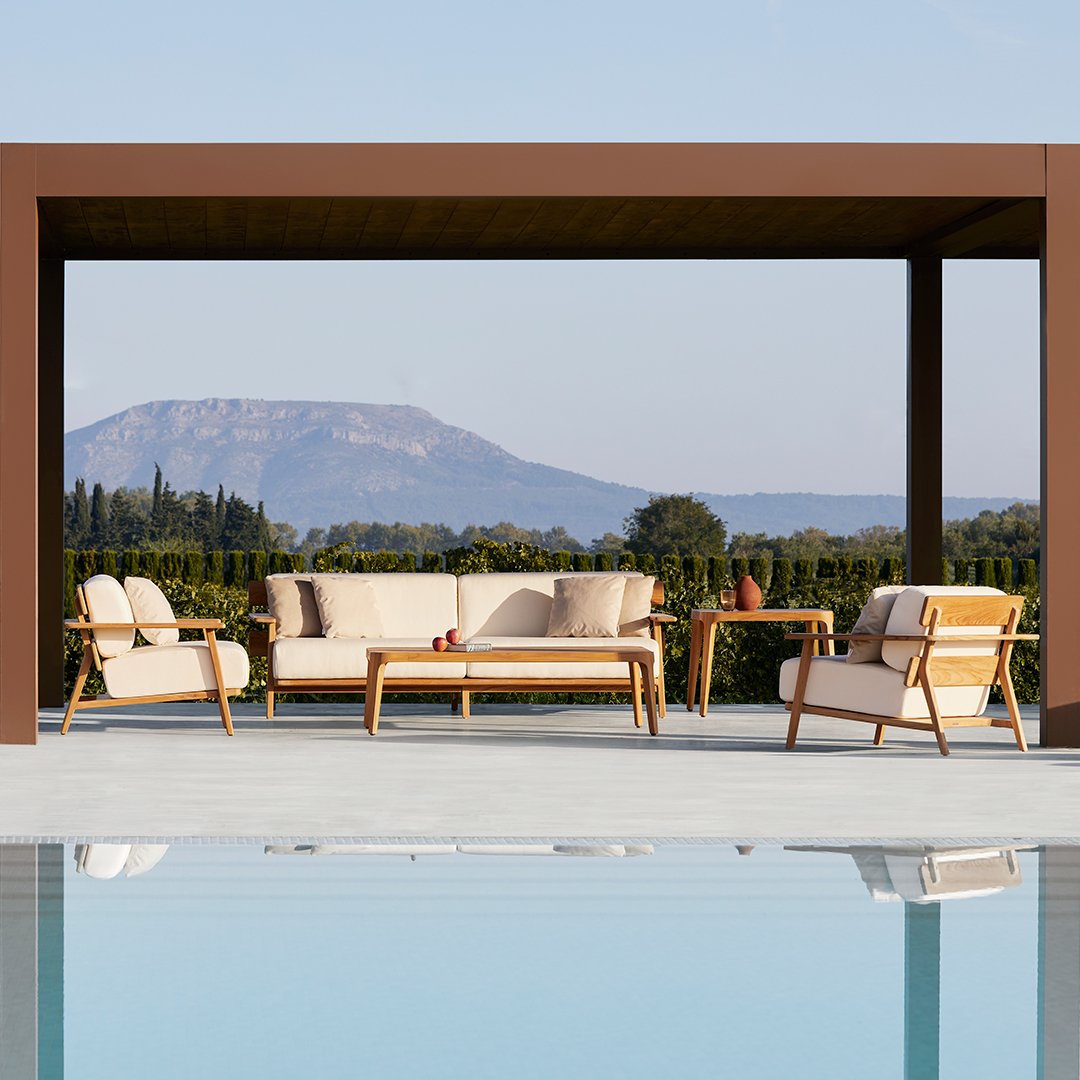 "Simple white lounge chairs with natural wood accents beside a tranquil blue pool, set against a green landscape."