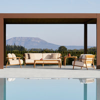 "Simple white lounge chairs with natural wood accents beside a tranquil blue pool, set against a green landscape."