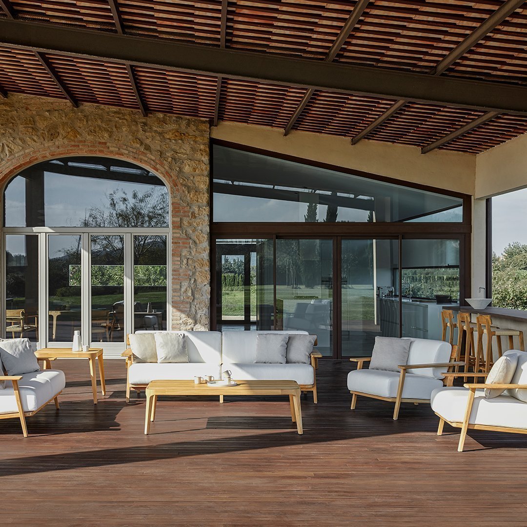 Elegant white cushions on natural wood frames, set against earthy stone and warm wooden tones in a modern outdoor setting.