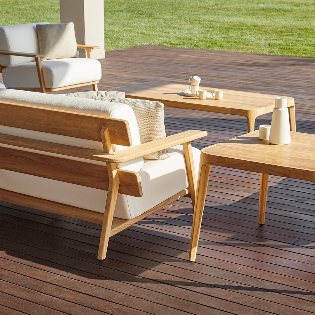 Natural wood finish with cream cushions and warm brown accents, set against a green lawn and wooden decking.