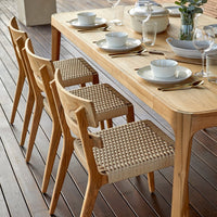 Natural wood dining table with woven beige chairs, accented by white plates and glasses for a warm, inviting setting.