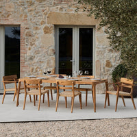 Wooden dining table set with natural wood finish, surrounded by stone and greenery. Elegant, modern outdoor decor.