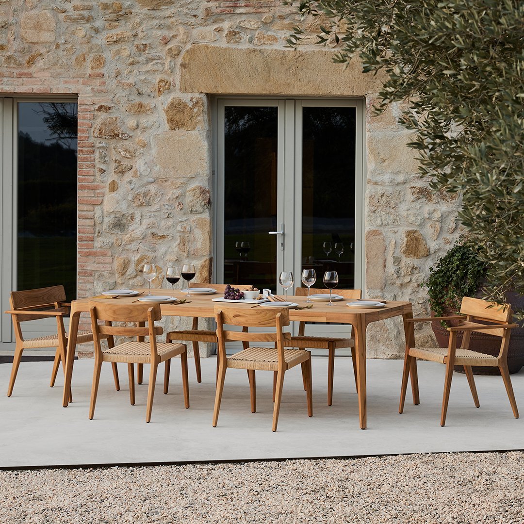 Stylish wooden dining set in natural wood tones, complementing a rustic stone wall backdrop. Elegant and inviting design.