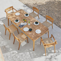 Natural wood dining table with woven chair patterns, complemented by white plates and vibrant greenery accents.
