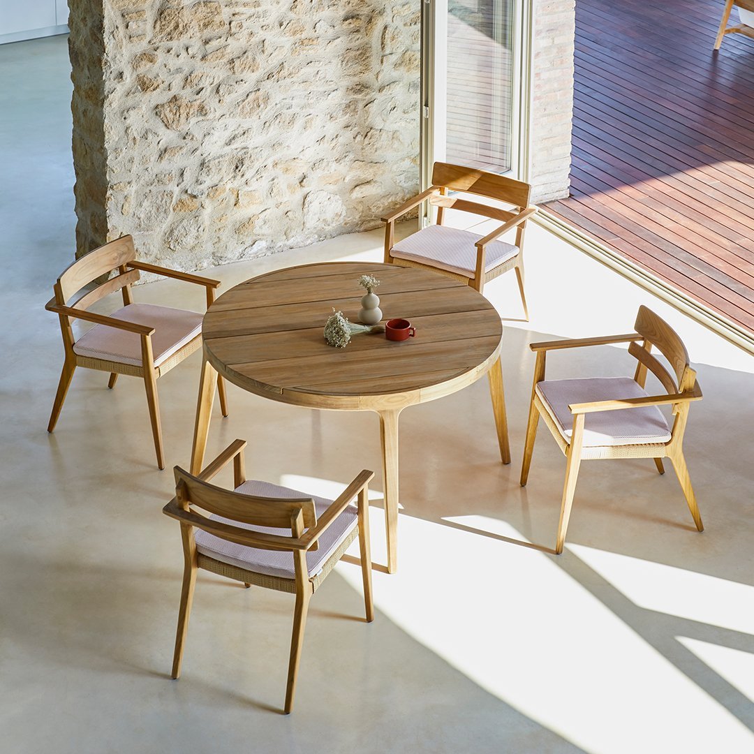 Natural wood round table with four light pink cushioned chairs, featuring a sleek, modern design and warm tones.