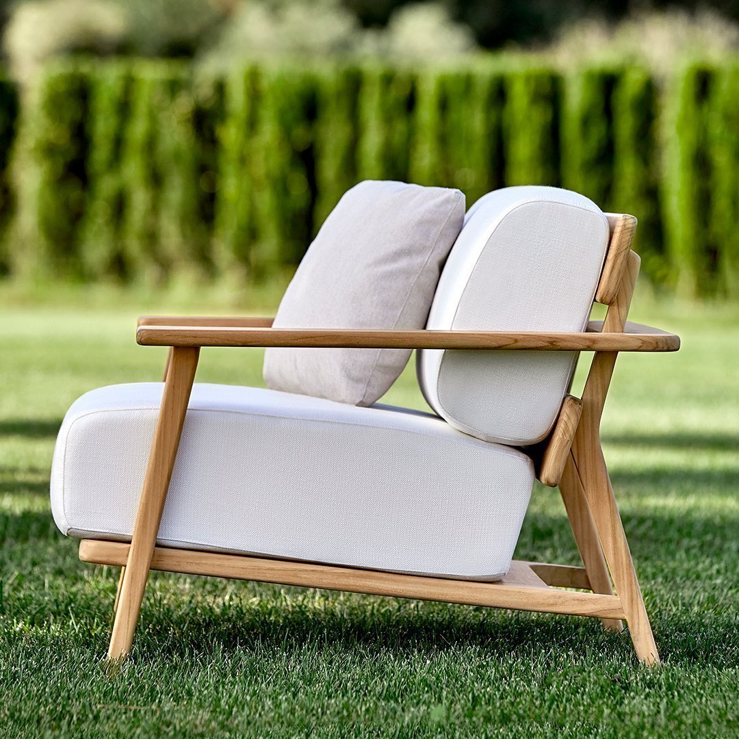 White outdoor chair with light beige cushions, featuring a modern design and natural wood frame against a grassy background.