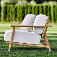 White outdoor chair with light beige cushions, featuring a modern design and natural wood frame against a grassy background.
